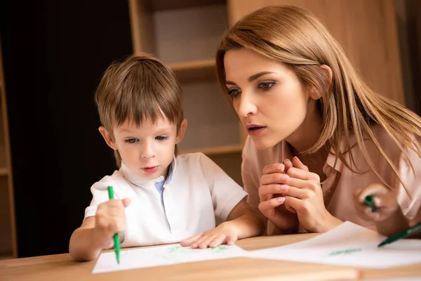 Educatore sorpreso guardando ragazzo disegno nella scuola materna — Foto stock