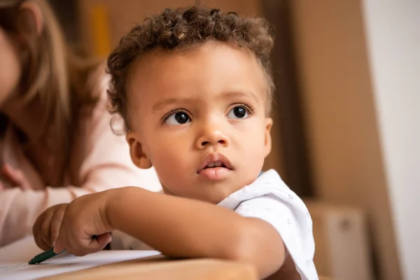 Porträt eines entzückenden afrikanisch-amerikanischen Jungen, der vom Tisch im Kindergarten wegschaut — Stockfoto