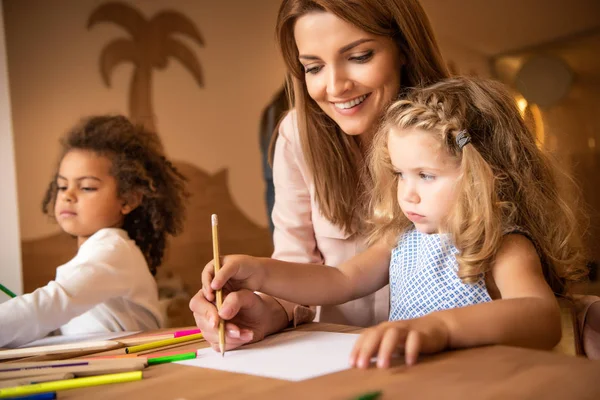 Tutor felice aiutare il bambino a disegnare all'asilo — Foto stock