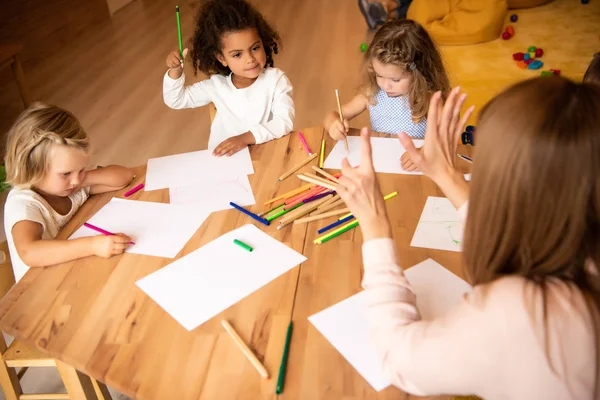 Tutor teaching multiethnic kids counting and showing number with fingers in kindergarten — Stock Photo