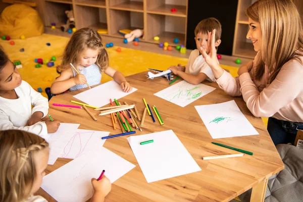 Éducateur souriant enseignant le comptage des enfants multiethniques et montrant le nombre avec les doigts dans la maternelle — Photo de stock