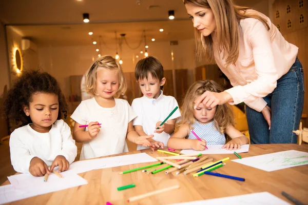 Educator looking at multiethnic children drawing in kindergarten — Stock Photo