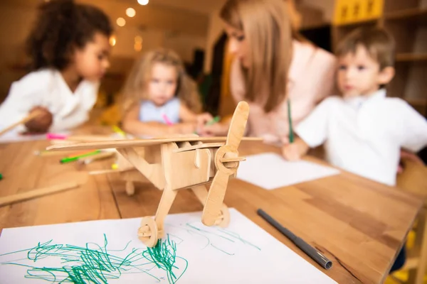 Educatore e bambini multiculturali disegno nella scuola materna, piano in legno in primo piano — Foto stock