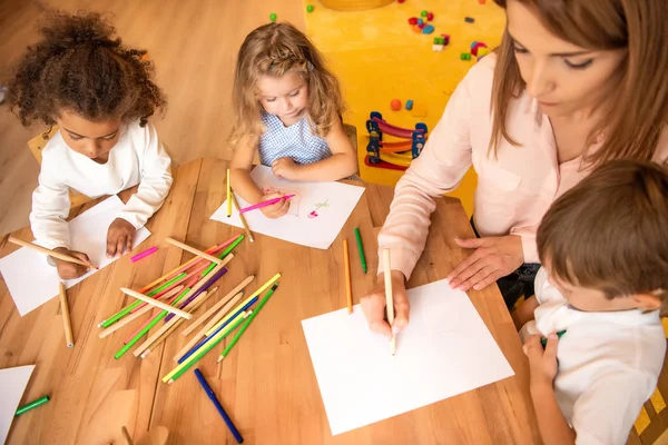 Visão de alto ângulo de educador e crianças multiétnicas desenho no jardim de infância — Fotografia de Stock