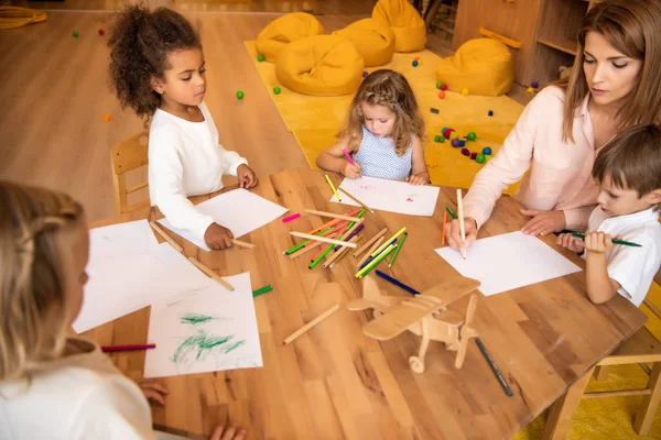 Vista ad alto angolo di educatore e bambini multiculturali disegno nella scuola materna — Foto stock