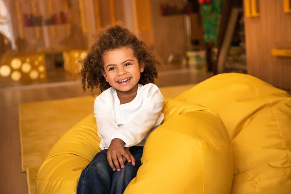 Sorridente adorabile bambino africano americano seduto sulla sedia sacchetto di fagioli nella scuola materna — Foto stock