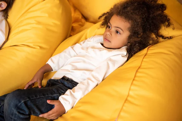 Blick aus der Vogelperspektive auf ein entzückendes afrikanisches amerikanisches Kind, das im Kindergarten auf einem Sitzsack-Stuhl liegt — Stockfoto