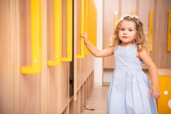 Lächelndes entzückendes Kind öffnet Spind in Kindergarten-Garderobe und blickt in die Kamera — Stockfoto