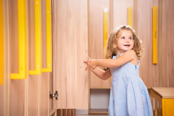 Smiling adorable kid opening locker in kindergarten cloakroom — Stock Photo