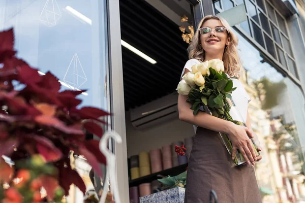 Low angle view of attractive florist going out from flower shop with roses in jar — Stock Photo