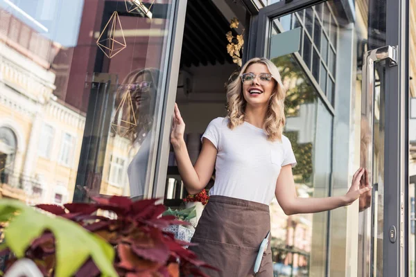 Low angle view of happy attractive florist opening door and going out from flower shop — Stock Photo