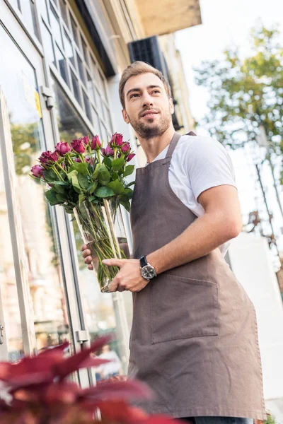 Low angle view of florist holding glass jar with burgundy roses near flower shop — Stock Photo