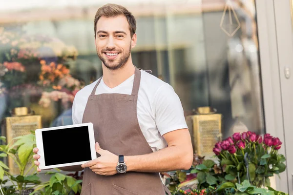 Sorridente bel fiorista che tiene tablet con schermo bianco vicino negozio di fiori e guardando la fotocamera — Foto stock