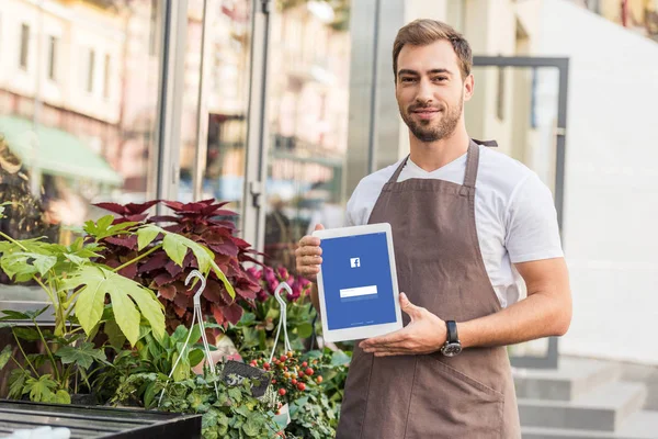 Handsome florist holding tablet with loaded facebook page near flower shop — Stock Photo
