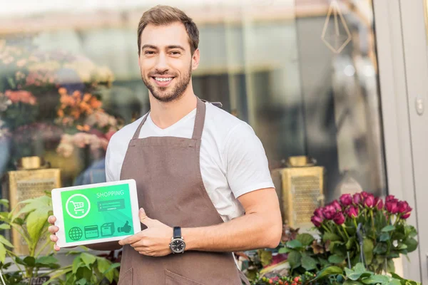 Smiling handsome florist holding tablet with shopping appliance near flower shop — Stock Photo