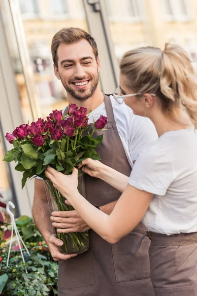 Happy young florists holding burgundy roses near flower shop — Stock Photo