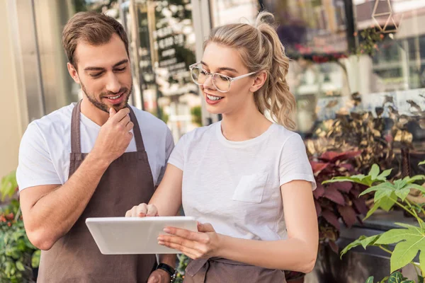 Fioristi sorridenti guardando tablet vicino negozio di fiori — Foto stock