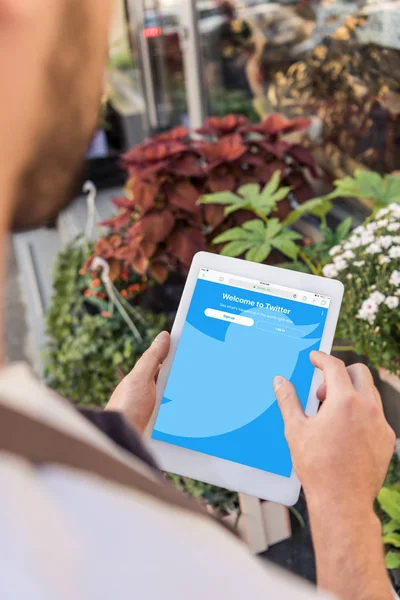 Immagine ritagliata di fiorista utilizzando tablet con pagina twitter caricato vicino al negozio di fiori — Foto stock