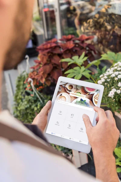Обрезанное изображение флориста с помощью планшета с загруженным квадратным листом возле цветочного магазина — стоковое фото