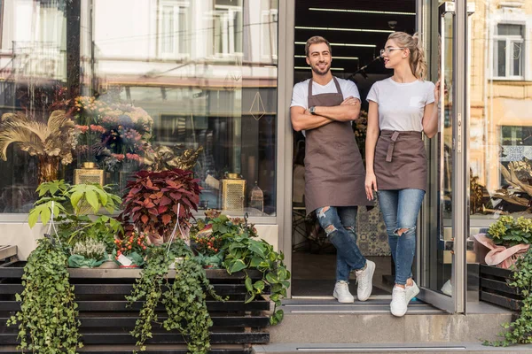 Улыбающиеся коллеги, стоящие в открытой двери цветочного магазина — стоковое фото