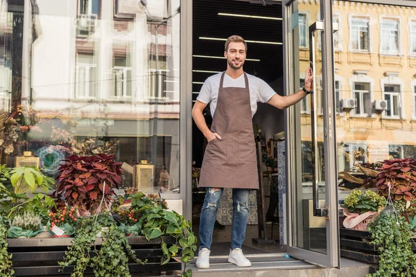 Floristería guapo en delantal apertura de la puerta de la tienda de flores - foto de stock