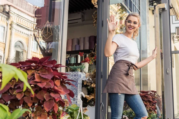 Attractive florist going out from flower shop and waving hand — Stock Photo