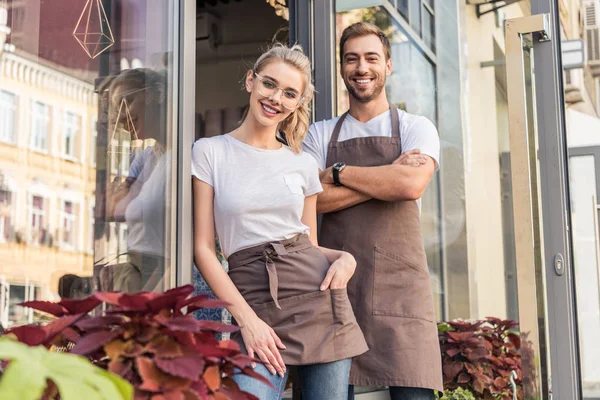 Smiling male and female florists standing near flower shop and looking at camera — Stock Photo