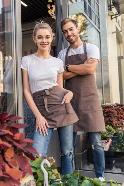 Smiling florists standing near flower shop and looking at camera — Stock Photo