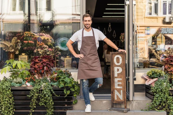 Sorridente bel proprietario del negozio di fiori in piedi sulle scale e appoggiato sul cartello aperto — Foto stock