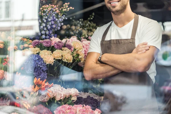 Обрізане зображення усміхненого флориста, що стоїть з схрещеними руками в квітковому магазині — стокове фото