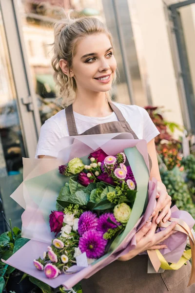 Attractive florist holding beautiful bouquet of chrysanthemums near flower shop and looking away — Stock Photo