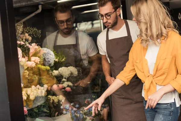 Customer pointing on flowers to florist at showcase in flower shop — Stock Photo