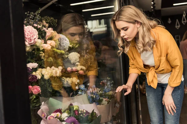 Attrayant fille regardant vitrine avec des fleurs au magasin — Photo de stock