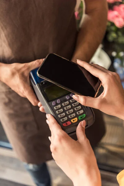 Обрезание изображения клиента, делающего бесконтактную оплату со смартфона в цветочном магазине — стоковое фото