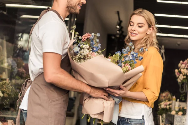 Florist giving wrapped bouquet to attractive customer at flower shop — Stock Photo