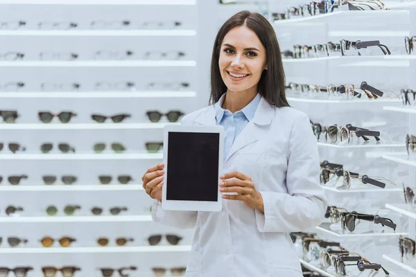 Attraktiver lächelnder Optiker zeigt digitales Tablet mit leerem Bildschirm im Augengeschäft — Stockfoto