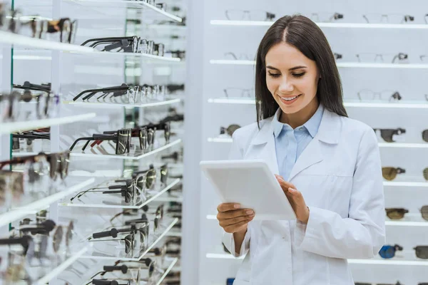 Professioneller Augenoptiker mit digitalem Tablet in der Nähe von Regalen mit Sehkraft in Optik — Stockfoto