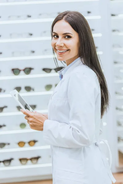 Улыбающийся оптик с помощью цифрового планшета на работе в офтальмологическом магазине — стоковое фото