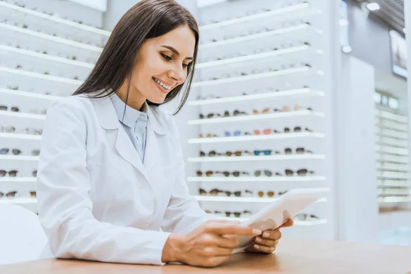 Professional smiling optician using tablet in optica — Stock Photo