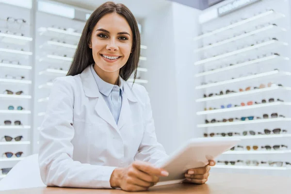 Schöne lächelnde Augenärztin mit digitalem Tablet im Augenoptikerladen — Stockfoto