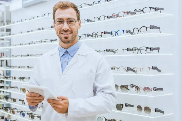 Profissional optometrista sorridente usando comprimido digital em óptica — Fotografia de Stock