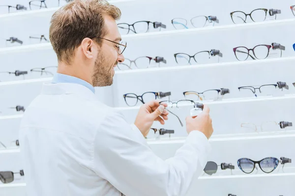 Oculist taking eyeglasses from shelves in ophthalmic shop — Stock Photo