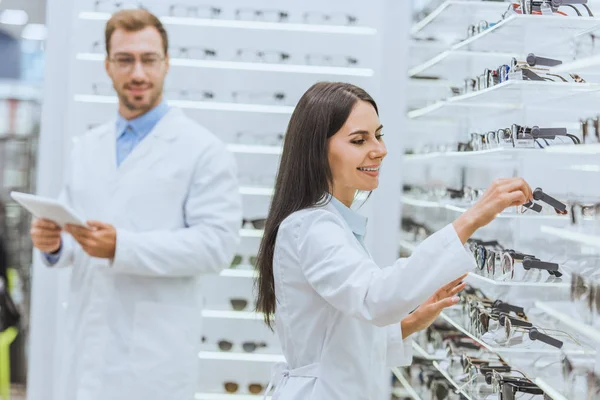 Два оптика, работающих и использующих цифровые таблетки в офтальмологическом магазине с очками — стоковое фото