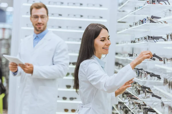 Two optometrists working and using digital tablet in ophthalmic shop with eyeglasses — Stock Photo