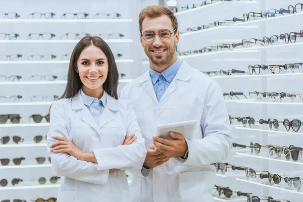 Two oculists with digital tablet looking at camera in optica — Stock Photo