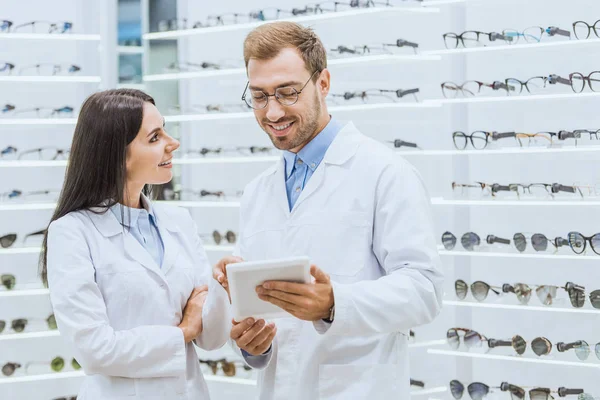 Zwei lächelnde Optometristen, die in der Optik mit einem digitalen Tablet arbeiten — Stockfoto