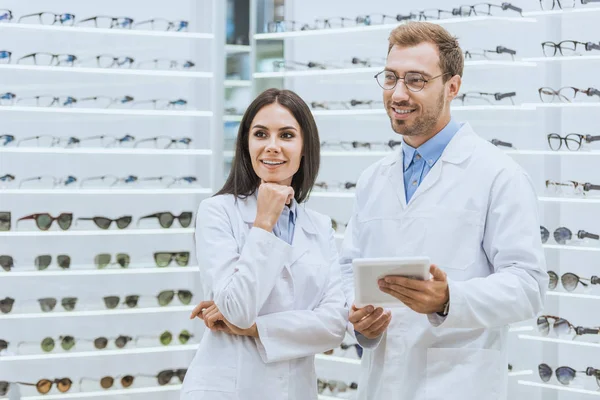 Zufriedene Augenoptiker bei der Arbeit und Nutzung digitaler Tablets in der Optik — Stockfoto