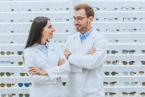 Ópticos profesionales felices en batas blancas posando con los brazos cruzados en oftalmología - foto de stock