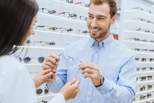 Partial view of female optometrist giving eyeglasses to happy man in optics — Stock Photo