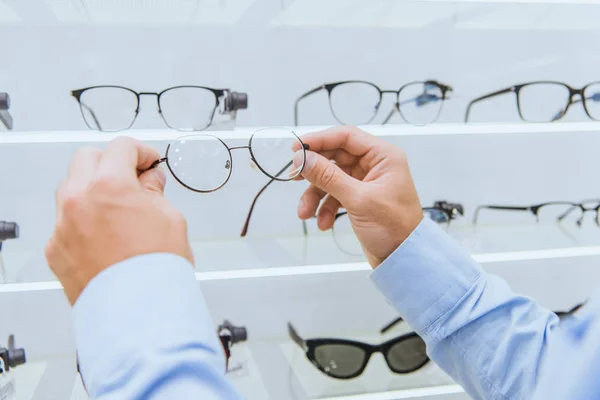 Cropped image of man taking eyeglasses from shelves in ophthalmic shop — Stock Photo